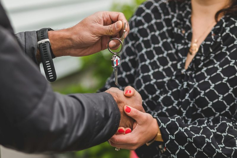 Hands exchanging a shiny house key against a blurred background, conveying a sense of new home ownership.