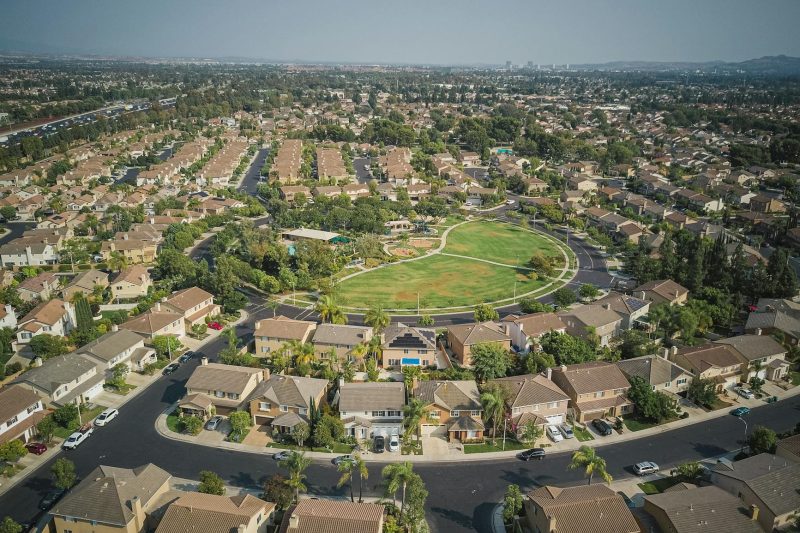 Aerial view of a spacious suburban neighborhood featuring houses, tree-lined streets, and a central park area.