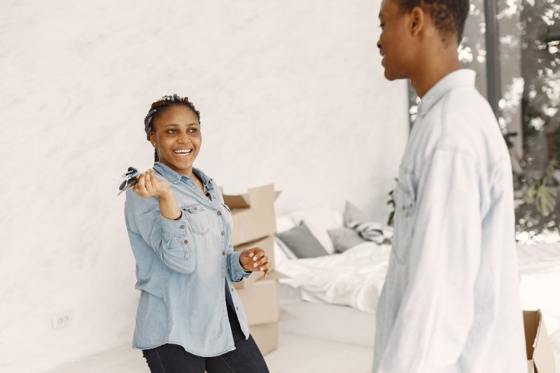 Smiling couple indoors holding a set of house keys, ready to move into their new home.