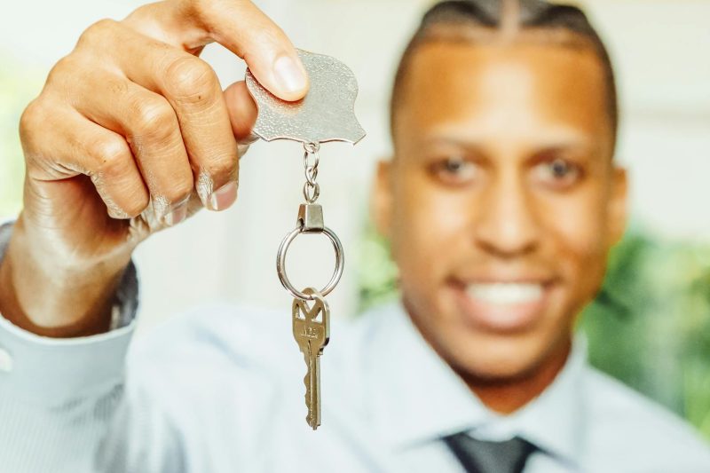 A cheerful real estate agent holds a house key, smiling, in a bright indoor setting.