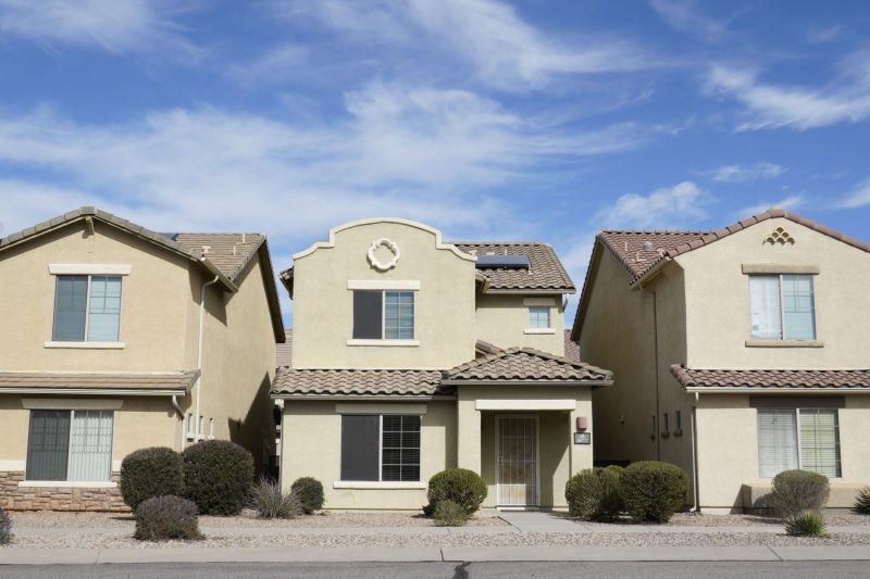 Three adjacent houses in a Tucson suburb under a clear blue sky.