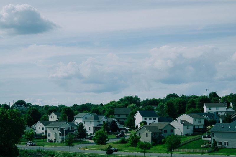 Picturesque suburban houses with well-maintained lawns under a blue sky with fluffy white clouds.