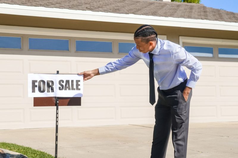 Professional real estate agent placing a "For Sale" sign in front of a suburban house.